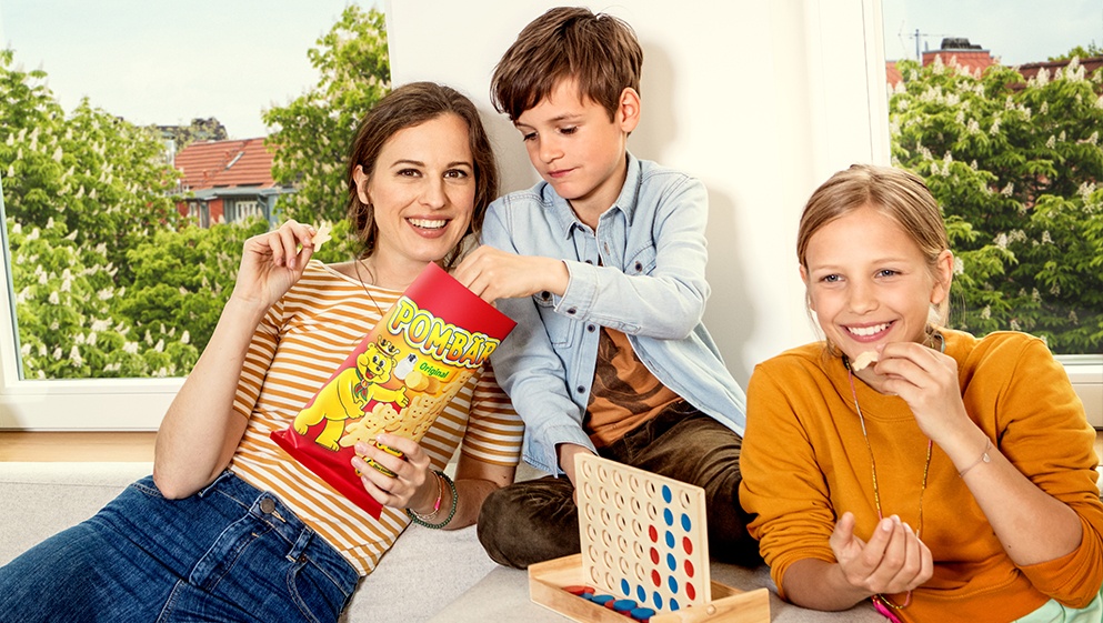 Eine Mutter spielt mit ihrem Sohn und ihrer Tochter, dabei snacken sie POM-BÄRen
